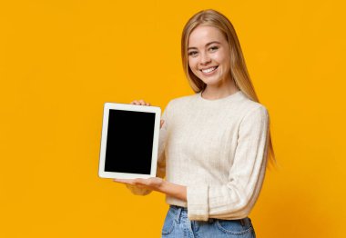 Portakal rengi stüdyo arka planında boş ekranlı dijital tablet tutan güzel bir genç kız.