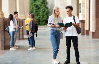 Gençler derslere hazırlanıyor, açık havada üniversite kampüsünde kitaplarla ders çalışıyor.
