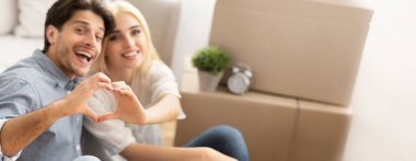 Sevgi dolu koca ve eş, yeni evdeki taşınan kutuların arasında oturan elleri ile kalp şeklinde hareket ediyor. Ev Sahipleri Konsepti, Boşluğu Kopyala