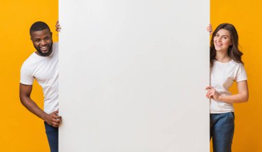 Sarı arka planda duran mutlu ırklar arası çiftin büyük beyaz reklam panosu mesajınız için bedava alan, panorama