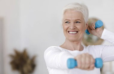 Evde Dambıllarla Egzersiz Yapan Aktif Yaşlı Kadın portresi, Boşluğu Kopyala