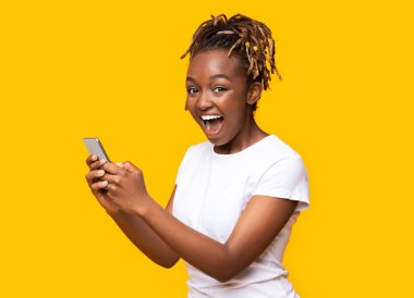 Sarı arka planda cep telefonu kullanan heyecanlı siyahi kadın, yeni bir uygulama aldı, boşluğu kopyaladı