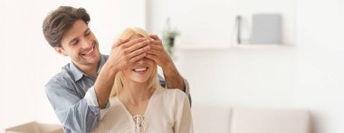 Neşeli bir adam bir kadının gözlerini arkadan kapar ve hoş bir sürpriz yaratır. Modern, aydınlık bir odadalar, birlikte neşeli bir anı paylaşıyorlar, kahkaha ve heyecanla dolu, kopyalama alanı