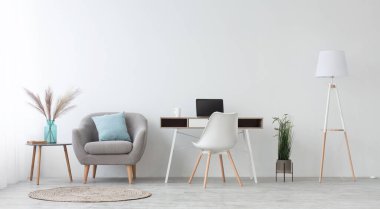Evdeki ofis, dolap ya da işyeri uzaktan çalışma için. Dizüstü bilgisayarı, beyaz koltuğu, mavi yastıklı koltuğu ve vazolu masası ve kuru bitkileri olan bir masa. Gün ışığında aydınlık duvarlar, panorama