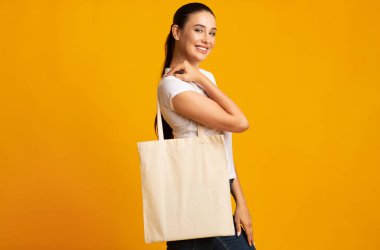 Plastik Kirliliği Durdur. Stüdyoda, sarı arka planda beyaz bir çanta tutan kadın. Metin için Boş Alan