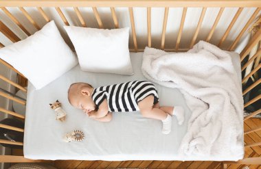 Tahta karyolada yan yatmış şirin bebek manzarası.