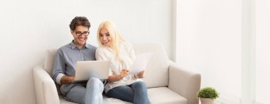 Genç bir çift hafif bir kanepede oturuyor, gülümsüyor ve dizüstü bilgisayarla meşgul. İçeriği incelerken keyifli anları paylaşıyorlar, yaşam alanlarında sıcak ve rahat bir atmosfer yaratıyorlar..