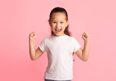 Kazan Kavramı. Heyecanlı Asyalı çocuk portresi, ellerini kaldırıp pembe arka planda yumruklarını sallıyor.