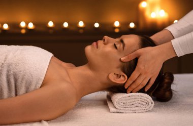 Romantik atmosferde modern lüks kaplıcalarda akupunktur masajı yaptıran neşeli genç bir kadın. Spa terapisti, genç ve güzel bir bayanın kafasına masaj yapıyor.