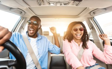 Yaz Tatilleri ve Yolculuk Konsepti. Heyecanlı siyah bir çiftin ön manzara portresi. Güneş gözlüklü, araba süren, müzik eşliğinde dans eden ve en sevdiği şarkıyı söyleyen, dinlenmek ve dinlenmek için tatile çıkan, güneşlenmek isteyen.