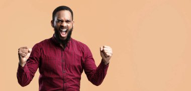 Şanslı Kişi Konsepti. Afrikalı Amerikalı bir adamın yumruklarını sıkarak çığlık attığı bir stüdyo resmi. Sakallı adam tezahürat yapıyor, el kaldırıyor, zaferi kutluyor.