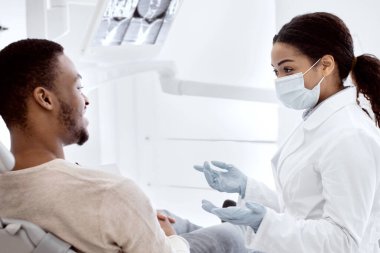 Afro-Amerikalı Stomatolog Kadın Diş Sağlığı Kliniğinde Erkek Hastayla Tedavi Sürecini Tartışıyor, Profesyonel Diş Doktoru Genç Siyah Adam 'a Danışmanlık Yapıyor, Kapalı Çekim