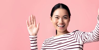 Hoş geldiniz. Neşeli genç Asyalı kadın selfie çekiyor ve kameraya el sallıyor arkadaş canlısı Koreli kadın fotoğraf çekerken jest yapıyor Pembe Stüdyo 'nun arka planında poz veriyor, fotokopi Alanı ile yakın çekim yapıyor.