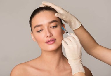 Plastik Cerrahi ve Güzellik Enjeksiyonu Konsepti. Kırışıklıklar için botoks yaptıran genç bir kadın Stüdyo Duvarı 'nda izole edilmiş.