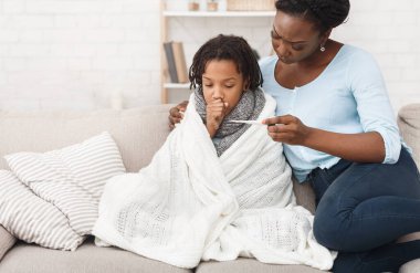 Afrikalı bir anne evde hasta çocuğunun sıcaklığını kontrol ediyor, battaniyeli bir kız.