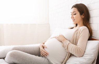 Active unborn baby pushing his mom, pregnant lady enjoying her pregnancy, lying in bed at home, copy space
