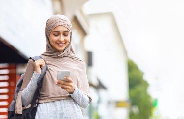 Sırt çantalı pozitif müslüman kız şehrin yanından geçerken akıllı telefon kullanıyor, boşluğu kopyala