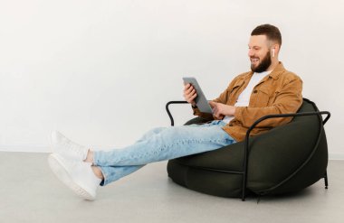 Bir adamın tablet bilgisayar ve kulaklık kullanırken görüntüsü ve kulaklıklar hafta sonları Beyaz Duvar 'ın üzerinde oturup internetten film izlerken. E-Öğrenme, İnternet ve Teknoloji Konsepti