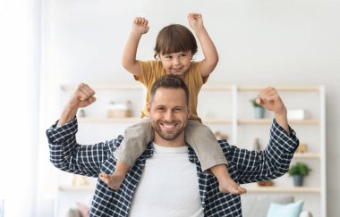 Aile gücü. Küçük oğlunu omuzlarında taşıyan, bisepslerini gösteren ve kameraya gülümseyen genç ve güçlü bir adam. Spor severler konsepti.