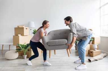Gülümseyen beyaz kadın ve koca, karton kutularla dolu bir odada koltuk taşıyorlar. Yeni eve taşınmak, mobilya almak. İpotek ve krediyle daire alıyor, emlak kiralıyor.