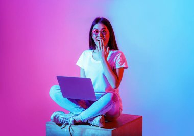 Çalışma alanında dizüstü bilgisayarı olan modern bir blogcu. Gözlüklü, ağzı kapalı, eli neonlu, stüdyo fotoğraflı şaşırmış bir kadın.