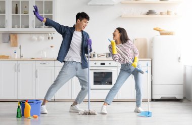 Komik Asyalı çift mutfağı temizlerken şarkı söylüyor, süpürge ve paspası mikrofon olarak kullanıyor, neşeli genç adam ve kadın rock yıldızlarını taklit ederken,