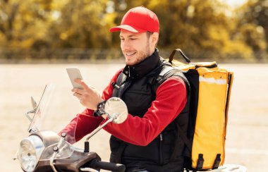 Yemek teslimatı. Moto Scooter 'da yemek dağıtımı için akıllı telefon uygulaması kullanan profesyonel kurye..