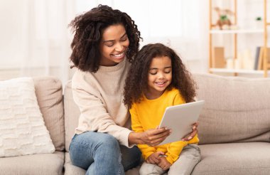 Anne ve kızının sevimli siyahi ailesi tablet bilgisayar kullanıyor evde kanepede oturup çizgi film izliyorlar..