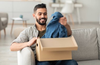 Mutlu bin yıllık Arap adam kutuları açıyor, başarılı alışverişlerden memnun, yeni giysiler çıkarıyor, evden sipariş alıyor. Çevrimiçi mağaza ve dağıtım kavramı