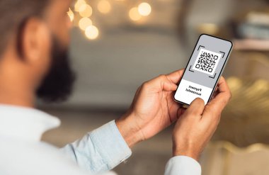 Cep telefonu ekranında QR kodu, yakın plan. Tanımlanamayan Afro-Amerikalı adam elinde barkodlu modern akıllı telefon tutuyor. Mal ve hizmetleri ödeme sistemiyle ödüyor. Yaratıcı imaj.