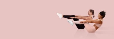 İki kadın, esnek ve güçlü olduklarını gösteren pembe bir zeminde senkronize çekirdek egzersizleri yapıyor. Her ikisi de düzgün bir şekilde odaklanıp kararlıdır..