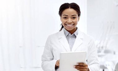 Beyaz önlüklü, dişçi kliniğinde poz veren mutlu siyah kadın dişçi portresi, Afro-Amerikan stomatolog kadın kameraya bakıyor ve gülümsüyor, panorama