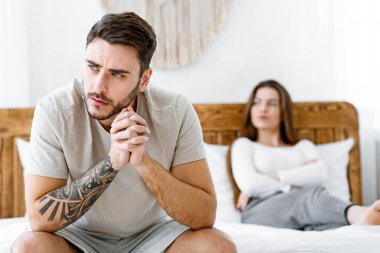 Aile krizi ve ilişki sorunları. Erkek ve kadın birbirlerine karşı stresli ve kızgın hissediyorlar, ahşap yatakta oturuyorlar ve modern etnik yatak odasının içinde, panoramada boş alana bakıyorlar.