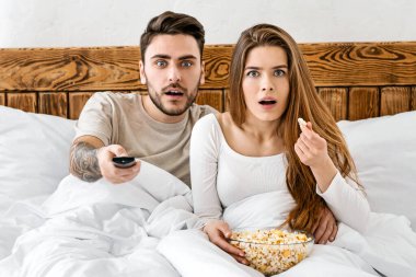 Akşamları film ve yatak konsepti. Şaşırmış karı koca televizyon izliyor ve patlamış mısır yiyor.