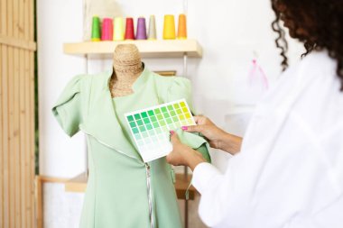 Dikiş ve tasarım konusunda yetenekli olgun bir İspanyol kadın, yaratıcı stüdyosunda şık yeşil bir elbise üzerinde çalışırken bir renk paletini eleştiriyor. Odaklanması sanatsal sürecini gösteriyor.