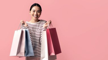 Neşeli Asyalı genç bayan portresi bir sürü parlak kağıt alışveriş torbalarıyla poz veriyor, neşeli bir milyon yıllık Koreli kadın sezonluk satışlardan ve büyük indirimlerden keyif alıyor, pembe arka planda tek başına duruyor.