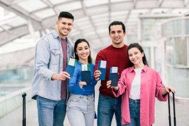 İki çiftten oluşan bir grup havaalanında gülümseyen seyahat belgelerini tutuyor. Birlikte tatile çıkacakları için heyecanlı görünüyorlar, ayrılmadan önce bir anlık eğlence ve macera sergiliyorlar..