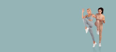 İki kadın spor yapıyor, uyumlu tayt giyerken spor pozları veriyorlar. Arkaplan, hareketlerini vurgulayan ve egzersize odaklanan katı bir renktir..