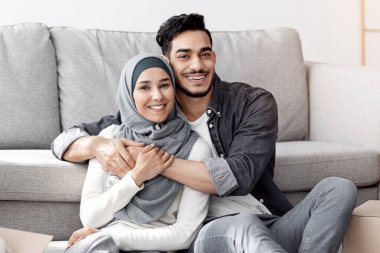 Güzel bir orta doğu çifti taşındıktan sonra bavullarını yerleştirirken dinleniyor, tesettürlü mutlu Arap adam ve kadın oturma odasındaki kağıt kutuların arasında oturuyor, sarılıyor ve gülümsüyor, boşluğu kopyalıyor.