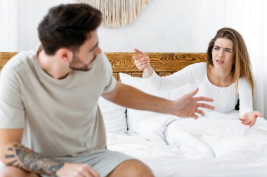 Covid-19 karantinasındaki ailede skandal ve sosyal sorunlar. Milenyum evli çifti stresli ve kızgın hissediyor, modern yatak odasında yatakta küfrediyor ve jest yapıyor. Gündüz vakti iç mekanda, boş alanda.