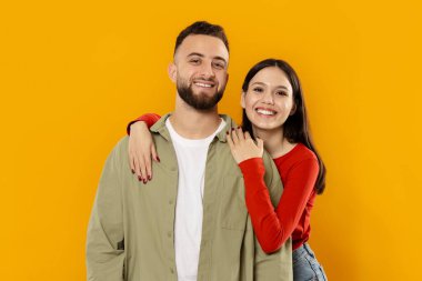 Neşeli genç bir çift, canlı sarı bir arkaplan arasında sırıtarak birbirlerini kucaklıyor. Birlikteliklerinin tadını çıkarırlarken mutluluk ve sıcaklık yayıyorlar..