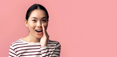 Ağız kenarında el ele tutuşan güzel Asyalı Kadın, Kameradaki Haberleri ya da Dedikoduları Paylaşan Genç Koreli Kadın Pembe Arkaplan 'ın üstünde Tek Başına Dururken Sırlarını Söylüyor, Yakın plan Çekimi, Kopyalama Boşluğu