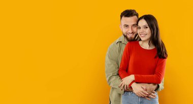 Genç bir çift birbirini kucaklıyor, mutluluk saçıyor. Parlak sarı bir duvarın önünde bir araya gelirler, sevgilerini ve bağlantılarını neşeli bir anda gösterirler, uzayı taklit ederler.