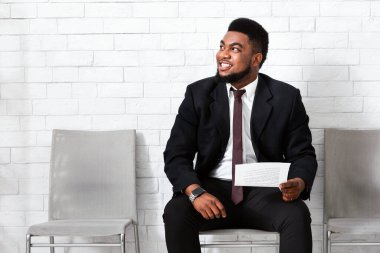 Takım elbiseli mutlu siyah adam şirket binasında iş görüşmesini bekliyor.