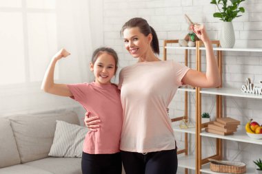 Gülümseyen anne ve genç kızının spor giyim kuşağındaki portresi kaslarını gösteriyor, evde gücünü gösteriyor. Kapalı devre süresince ev içi sağlık konsepti