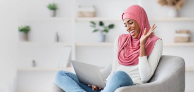Uzaktan iletişim. Keyifli İslamcı kadın evde dizüstü bilgisayarla video görüşmesi yapıyor, neşeli dindar Afrikalı kadın bilgisayar kamerasına el sallıyor, online toplantıdan keyif alıyor, uzay kopyaları kopyalıyor.