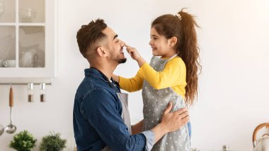 Orta Doğulu bir baba ve küçük bir kız mutfakta kurabiye pişirirken eğlenirken, sevimli bir kız çocuğu, babasına dokunuyor, gülüyor ve babasıyla eğleniyor.