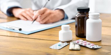 Haplara odaklan. Ofisteki doktor hastaya ilaç yazıyor.