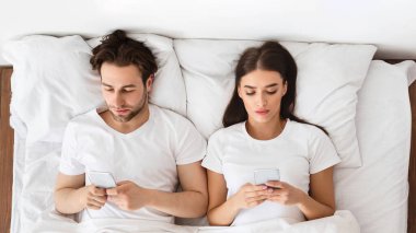 Evdeki yatakta uzanan cep telefonlarını kullanan çiftlerin en iyi görüntüsü. Karı koca sevgilileriyle mesajlaşırken birbirlerini görmezden geliyorlar. İnsanlar ve Gadget 'lar, Evlilik Konseptinde İlgisizlik ve Sadakatsizlik