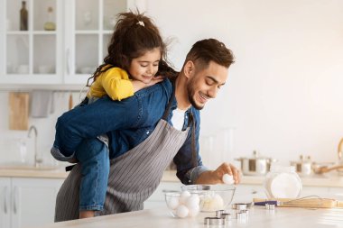 Genç Arap Baba 'nın portresi, tatlı küçük kızıyla mutfakta yemek pişirirken, Orta Doğulu bir babanın sevimli bir kızı sırtında taşırken, evde pastayı hazırlarken,